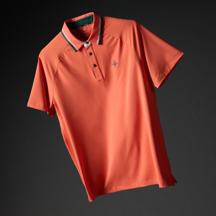 Coral orange golf polo shirt with green and white striped collar and embroidered compass logo on a dark background