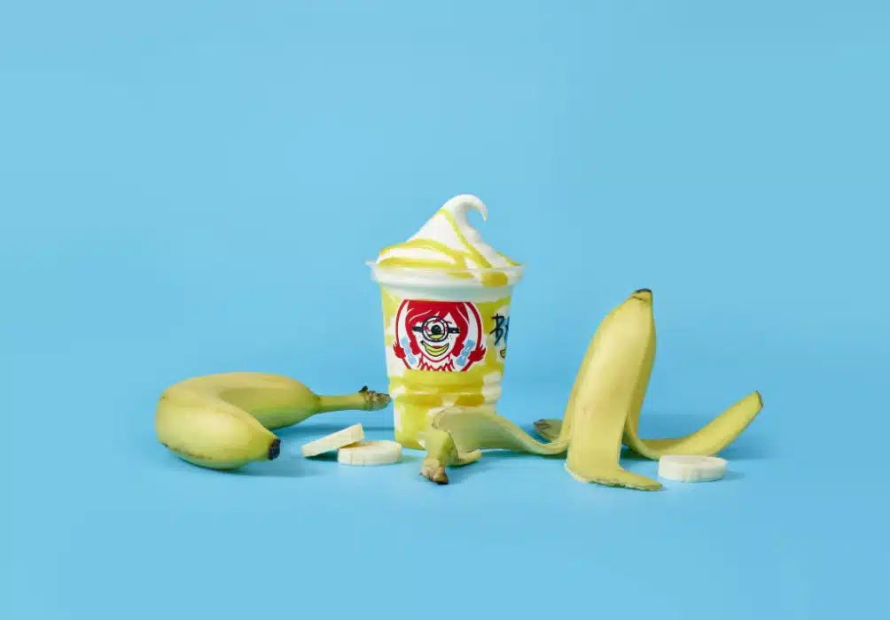 Banana Frosty Swirl in a branded cup beside a whole banana, banana peel, and banana slices against a blue background