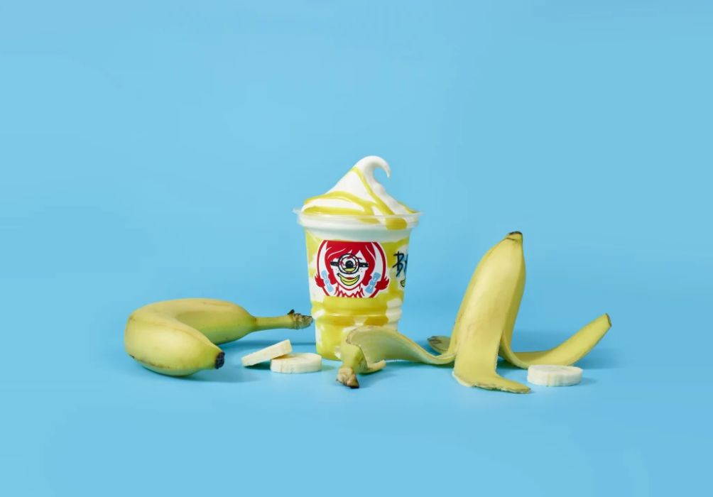 Banana Frosty Swirl in a branded cup beside a whole banana, banana peel, and banana slices against a blue background