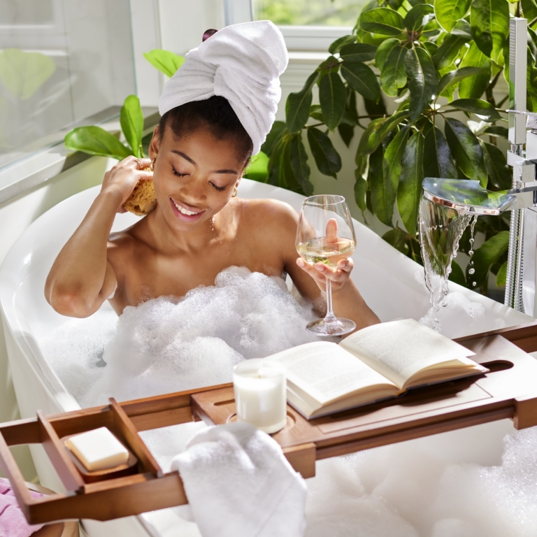 Woman with a towel wrapped around her hair relaxing in a bubble bath holding a glass of champagne