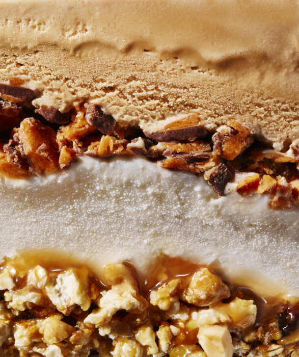 Extreme close-up cross-section of layered ice cream cake showing coffee and vanilla ice cream bands with chopped toffee and caramel popcorn filling