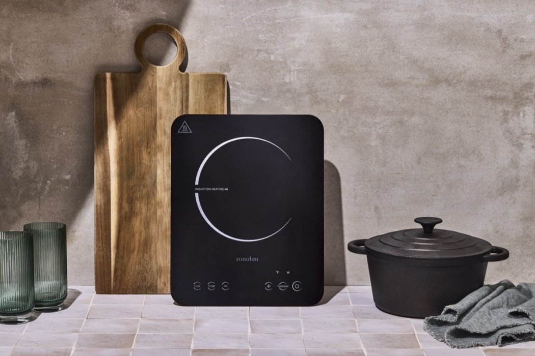 Black Zonohm portable induction cooktop standing upright showing a glowing circular heating indicator, styled with a wooden cutting board and dark cast iron Dutch oven