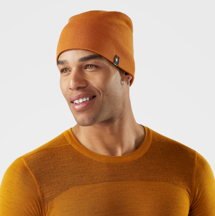 Male model wearing an orange knit beanie and performance shirt photographed on white.